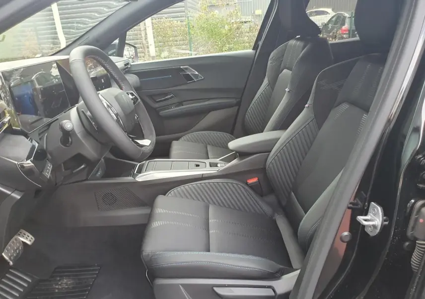 Intérieur de la Renault Clio VI noire étoile, vue côté gauche, sièges avant en tissu avec surpiqûres bleues.