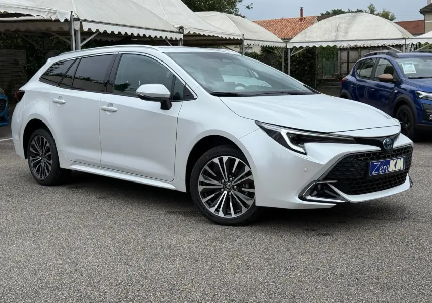 Toyota Corolla Touring Sport blanche nacrée vue en 3/4 avant côté gauche, avec jantes alliage et calandre noire distinctive.