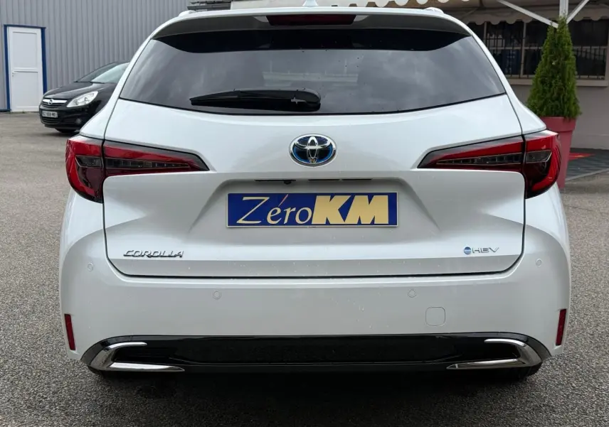 Vue arrière d'une Toyota Corolla Touring Sport blanche nacrée avec logo hybride et feux arrière rouges distinctifs.