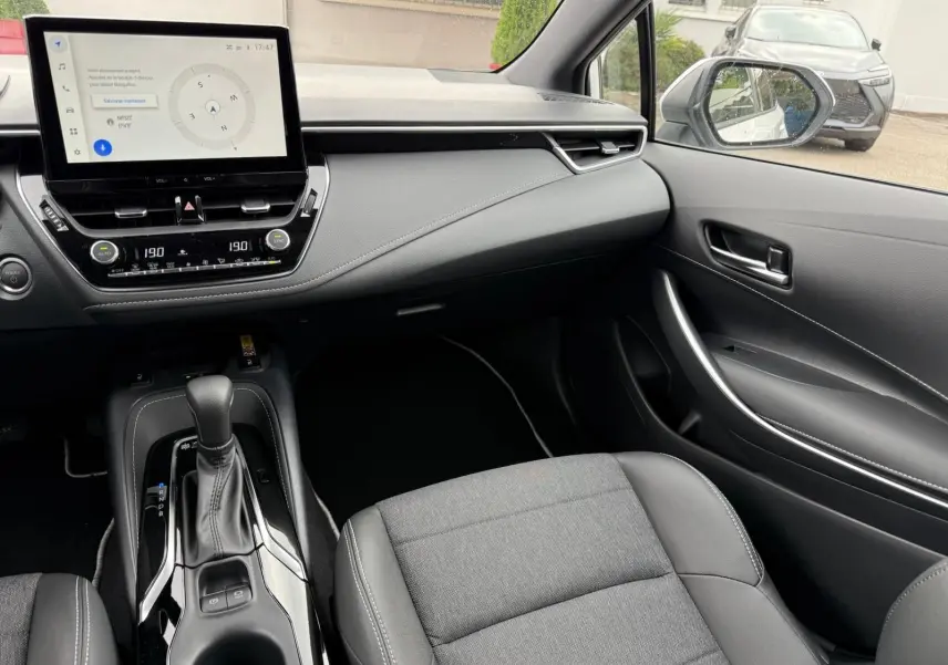 Intérieur de la Toyota Corolla Touring Sport 2025, vue côté passager, tableau de bord moderne et console centrale noire élégante.