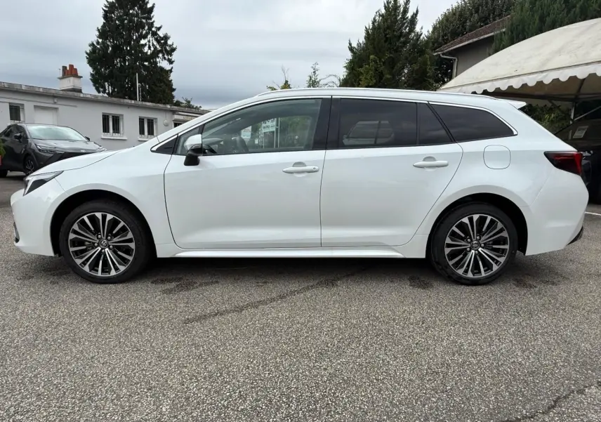 Profil côté gauche d'une Toyota Corolla Touring Sport 2025 blanc lunaire nacré avec jantes alliage noires et grises.