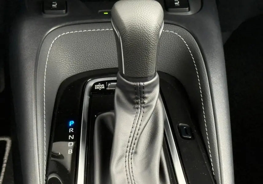 Gros plan sur le levier de vitesses automatique en cuir noir avec surpiqûres blanches de la Toyota Corolla Touring Sport blanche.