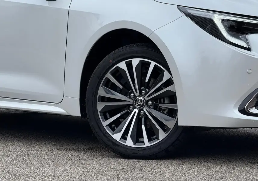 Gros plan sur la roue avant droite et le phare d'une Toyota Corolla Touring Sport blanc lunaire nacré.