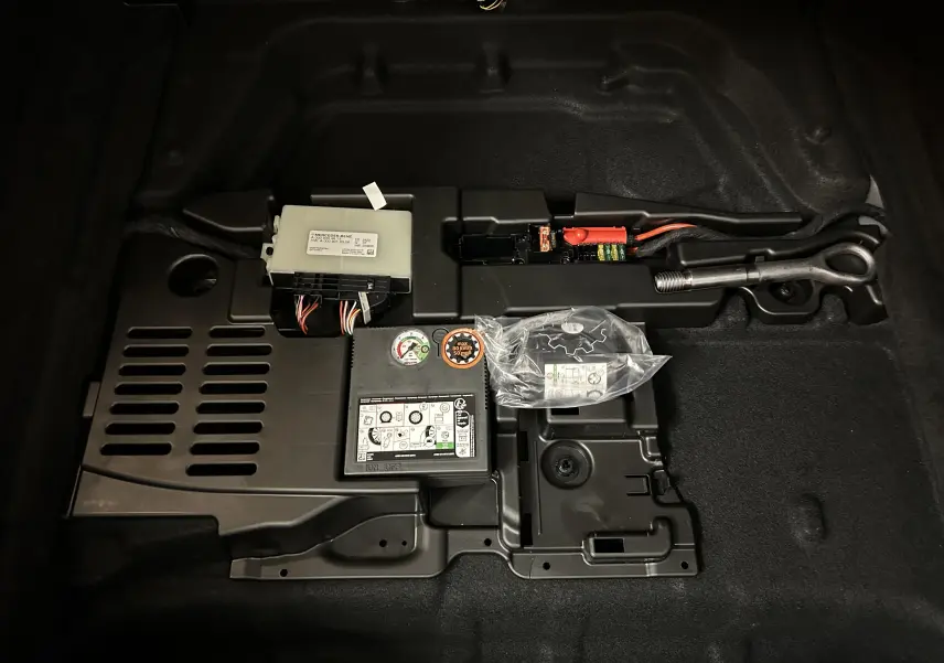 Vue rapprochée du compartiment de rangement sous le coffre d'une Mercedes CLA Shooting Brake noire, montrant outils et kit de réparation.