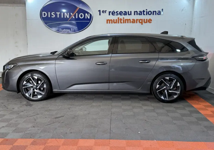Profil droit d'une Peugeot 308 SW gris foncé 2022, avec jantes alliage et toit noir, stationnée en intérieur showroom.