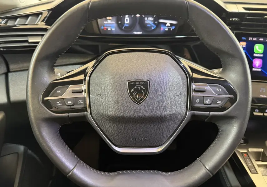 Vue rapprochée du volant cuir noir de la Peugeot 308 2022 avec commandes multifonctions et tableau de bord digital.