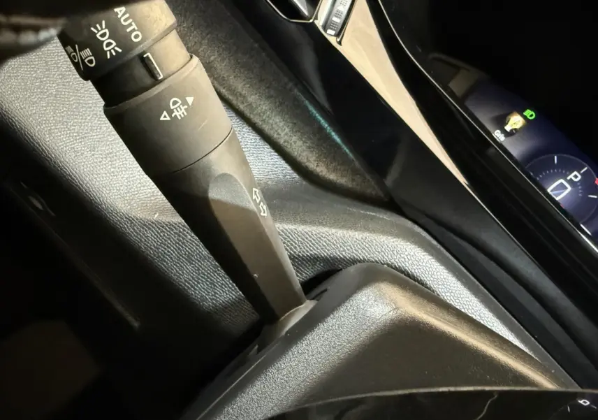 Gros plan sur la commande des feux et le tableau de bord digital bleu de la Peugeot 308 gris foncé, version 2022.