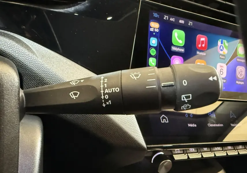 Gros plan sur la commande des essuie-glaces à gauche du volant, avec écran tactile affichant les applications du système multimédia.