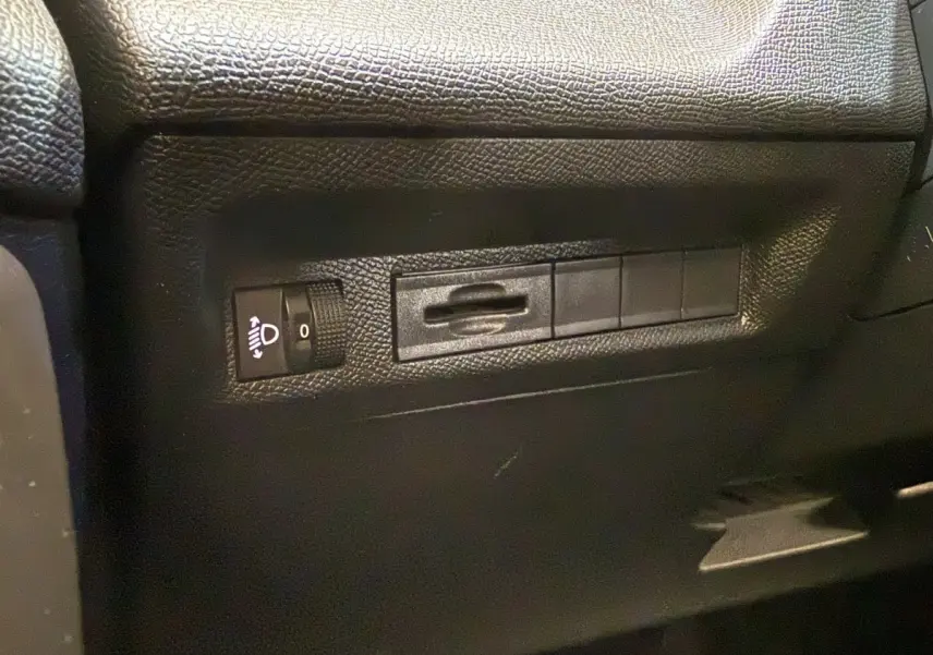 Détail intérieur montrant les commandes de réglage des phares sur le côté gauche du tableau de bord d’une Peugeot 308 gris foncé.