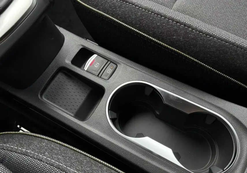 Gros plan sur la console centrale noire étoile du Renault Captur 2025, avec porte-gobelets et frein à main électrique.