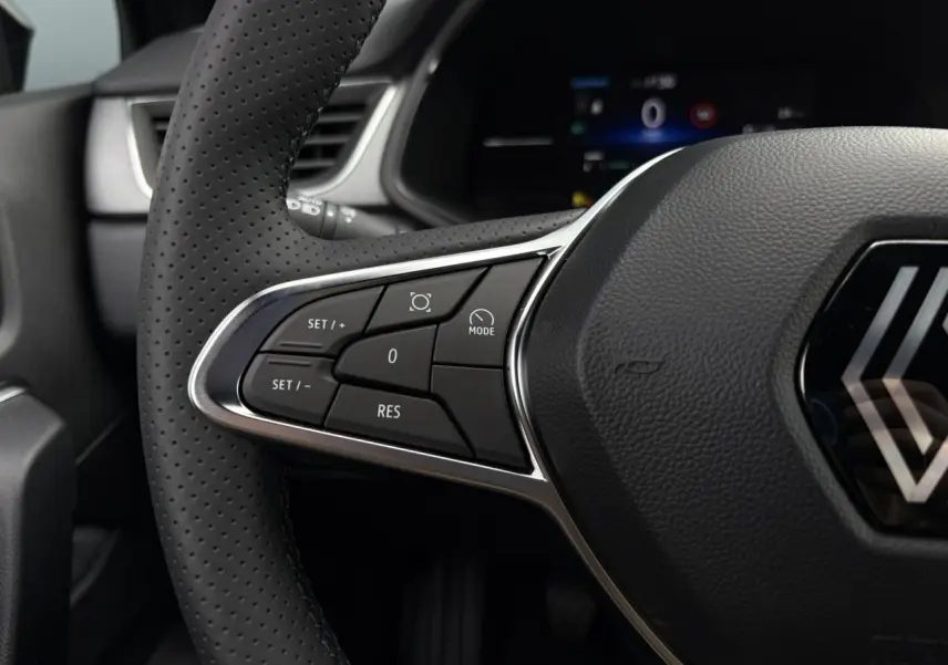 Gros plan sur le volant perforé noir du Renault Captur 2025 avec commandes intégrées et logo central chromé.