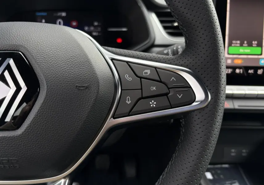 Gros plan sur le volant noir perforé du Renault Captur 2025 avec commandes intégrées et écran tactile en arrière-plan.