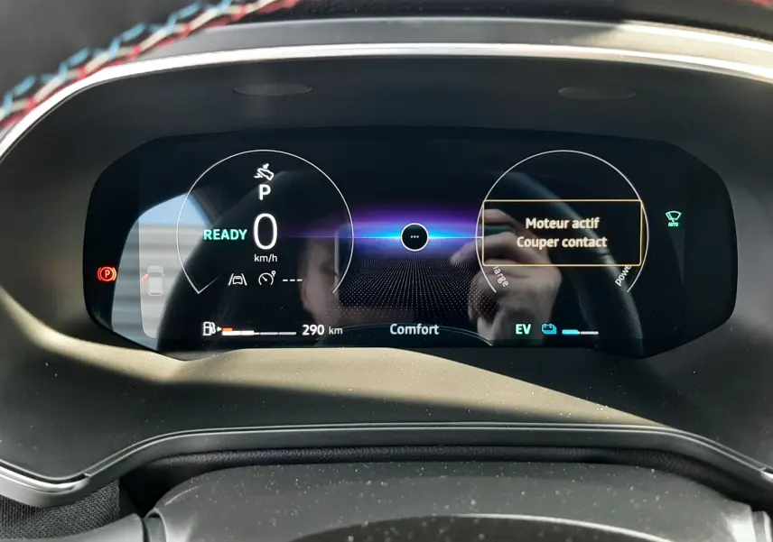 Tableau de bord numérique du Renault Captur 2024 hybride, affichant vitesse zéro et message moteur actif, vue frontale rapprochée.