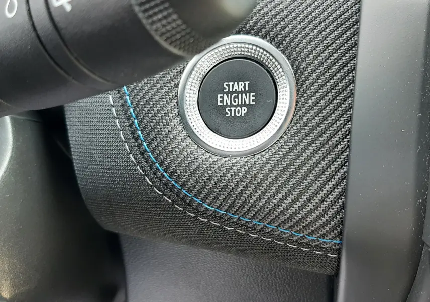 Bouton Start Engine Stop sur tableau de bord en tissu noir à surpiqûres bleues du Renault Captur 2024 hybride.