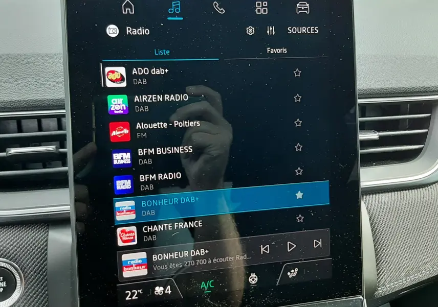 Écran tactile central du tableau de bord du Renault Captur 2024 affichant les stations radio DAB+ avec commandes climatisation en dessous.