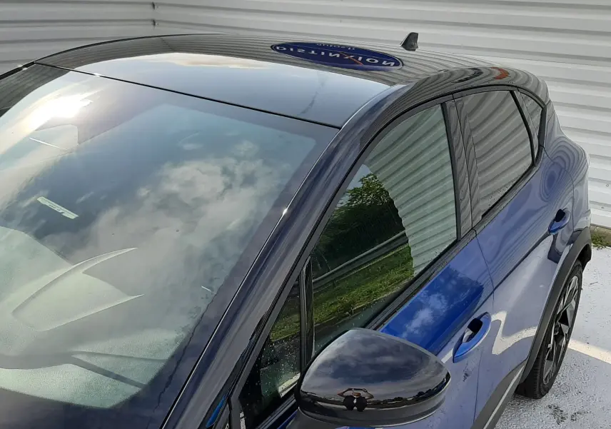 Vue plongeante côté gauche sur Renault Captur 2024 bleu Iron avec toit noir brillant et rétroviseur assorti.