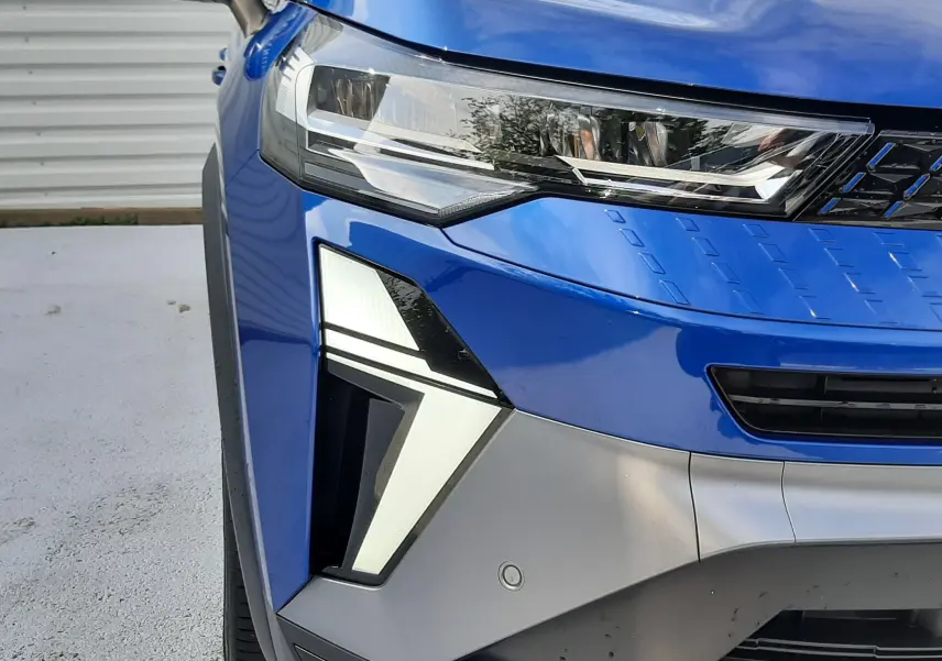 Gros plan sur l'avant gauche du Renault Captur 2024 bleu Iron avec feux LED au design angulaire et calandre noire.
