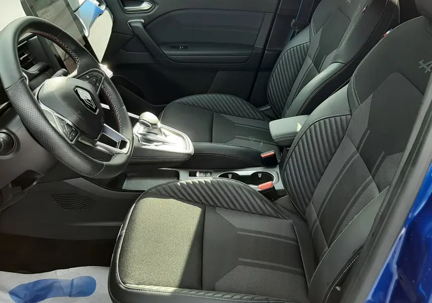 Vue intérieure côté conducteur du Renault Captur 2024 bleu iron, sièges noirs avec surpiqûres et volant multifonction.