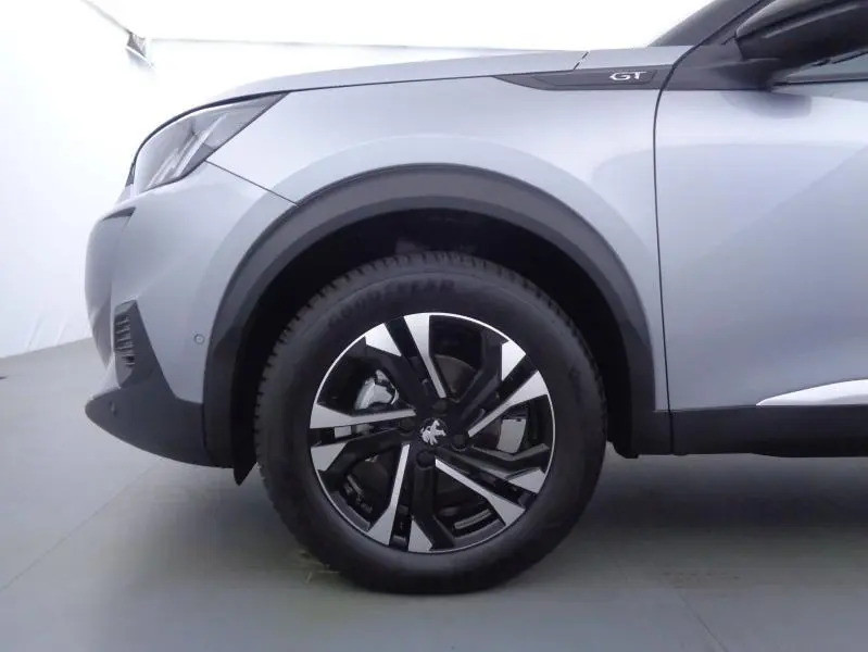 Gros plan sur la roue avant gauche et l'aile gris Artense du Peugeot 2008 GT avec jante alu bicolore.