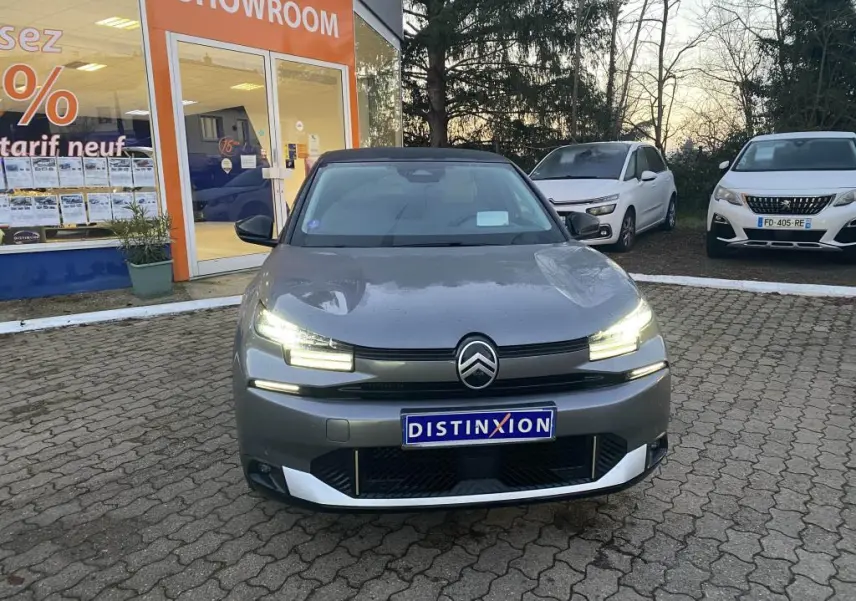 Citroën C4 gris foncé vue de face avec phares LED allumés et toit bi-ton noir devant un showroom.