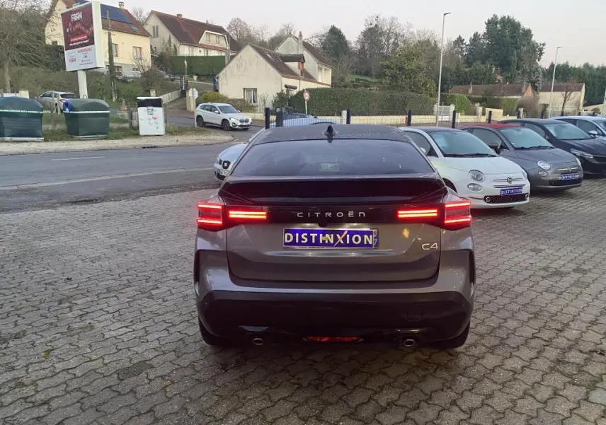 Vue arrière d'une Citroën C4 gris foncé avec toit noir, feux arrière LED allumés sur parking pavé.