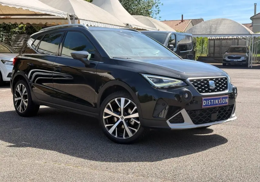 SEAT Arona noir vue 3/4 avant droit, avec jantes alliage et calandre distinctive sous un ciel ensoleillé.