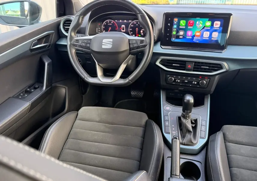 Intérieur du SEAT Arona 2022 vu de face, volant cuir, écran tactile central avec Apple CarPlay, sièges tissu noir.