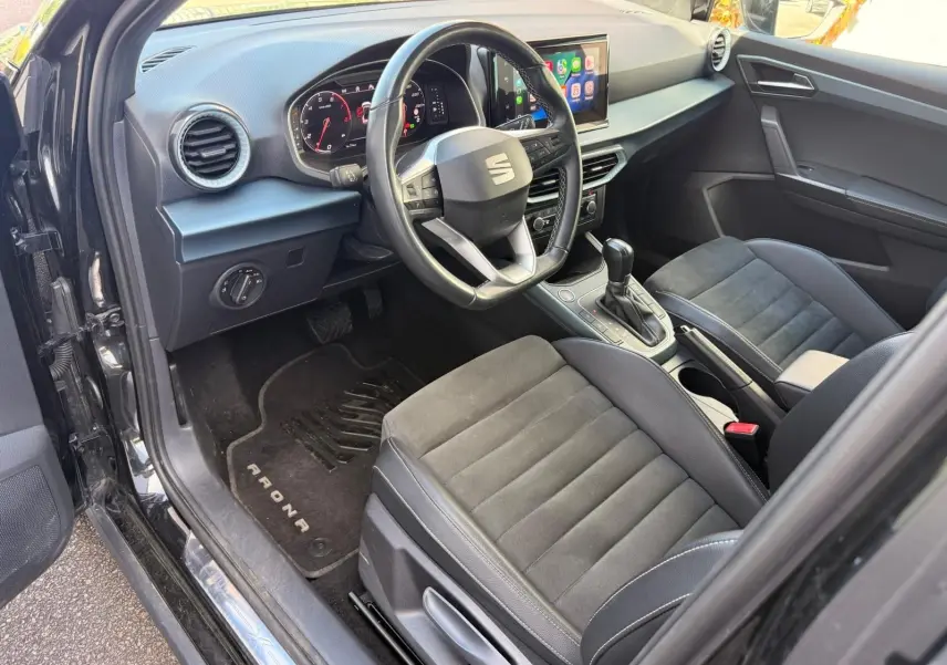 Vue intérieure côté conducteur du SEAT Arona 2022, avec sièges noirs, volant cuir multifonctions et écran tactile central.