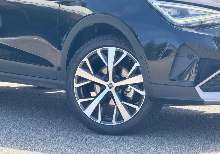 Gros plan sur la roue avant droite et partie avant d’un SEAT Arona 2022 couleur sombre avec jante alu bicolore.