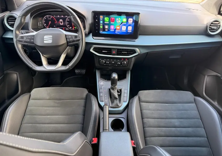 Vue intérieure avant du SEAT Arona 2022 avec tableau de bord moderne, écran tactile central et sièges noirs en tissu et cuir.