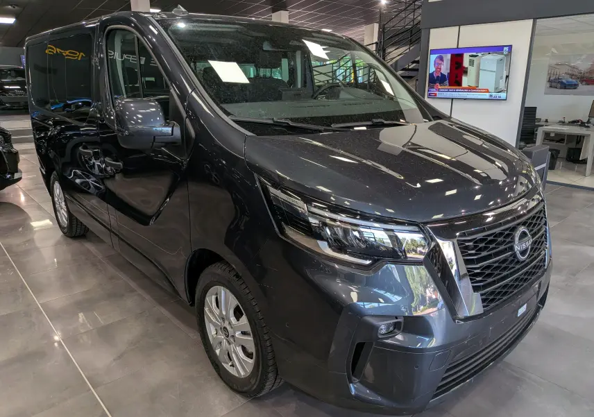 Vue 3/4 avant droit du Nissan Primastar Combi gris comète, mettant en valeur sa calandre chromée et ses phares modernes.