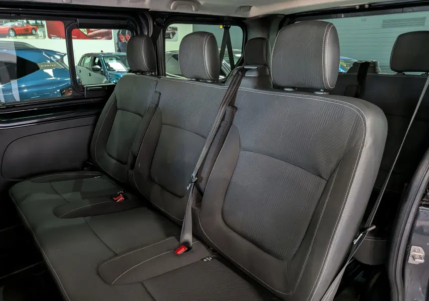 Vue intérieure des sièges arrière en tissu noir du Nissan Primastar Combi gris, montrant la banquette 3 places avec ceintures de sécurité.