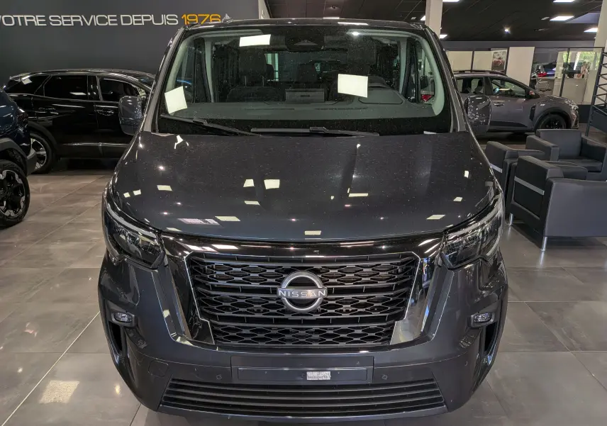 Vue frontale d'un Nissan Primastar Combi gris comète 2025, avec calandre noire et logo Nissan bien visible.