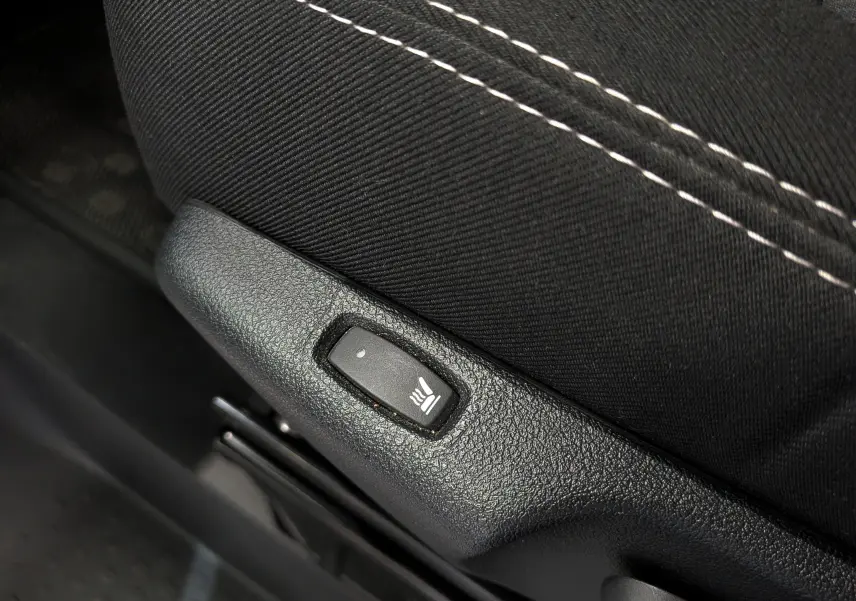 Détail du bouton de chauffage de siège sur la garniture noire avec surpiqûres blanches du Nissan Primastar Combi 2025.