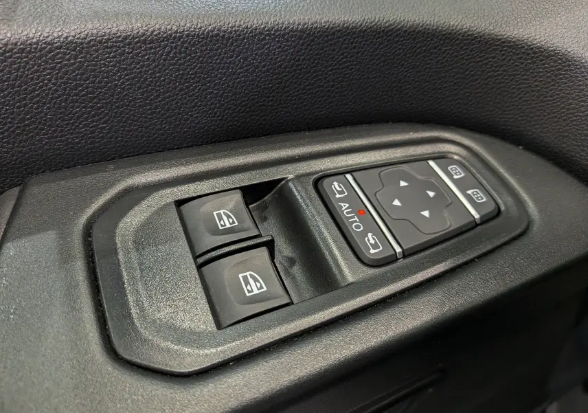 Gros plan sur les commandes de lève-vitres et réglages des rétroviseurs du Nissan Primastar Combi gris, côté conducteur.