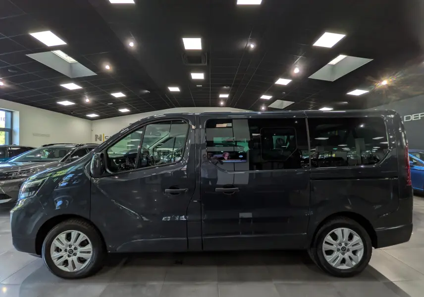 Vue de profil côté gauche du Nissan Primastar Combi gris comète 2025 en intérieur, avec vitres teintées et jantes alliage.