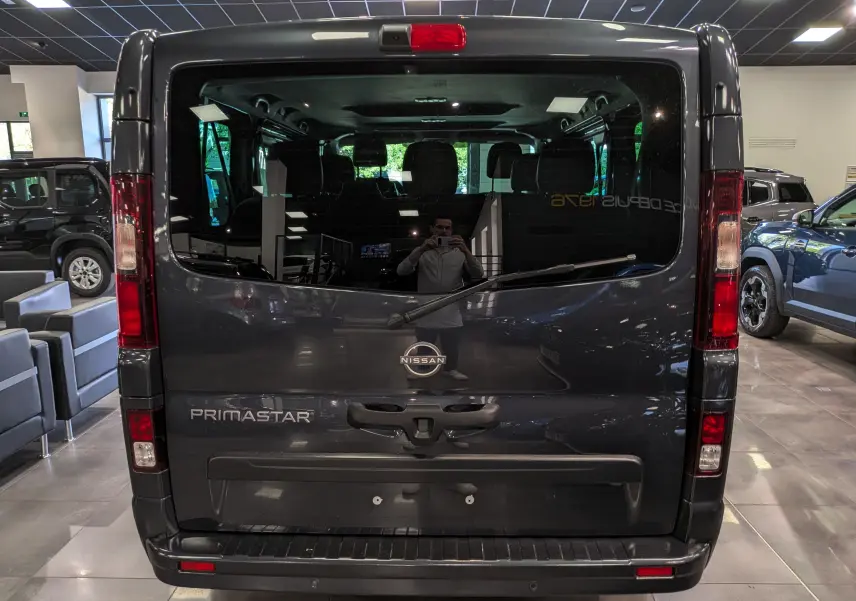 Vue arrière d’un Nissan Primastar Combi gris comète 2025, avec logo et nom du modèle visibles sur la porte arrière vitrée.