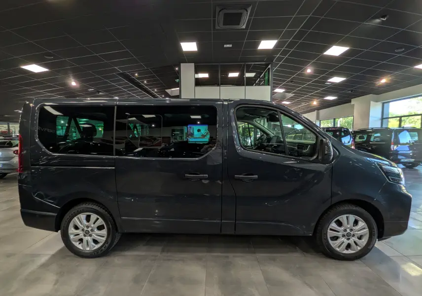 Vue de profil côté gauche d’un Nissan Primastar Combi gris comète 2025 dans un showroom lumineux.