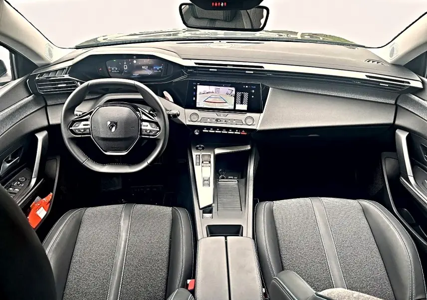Vue intérieure avant de la Peugeot 308 2025 noire, montrant volant multifonction, écran tactile et sièges tissu gris tremezzo.