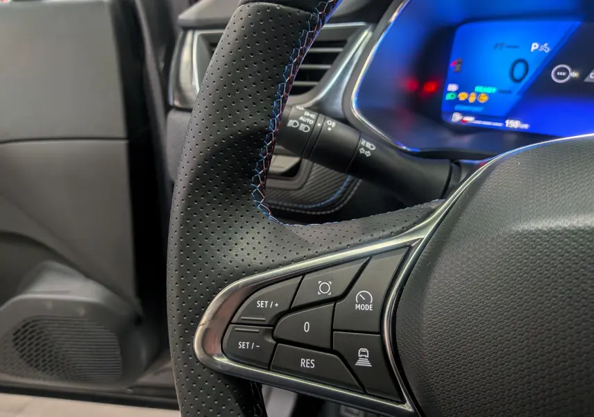 Gros plan sur le volant en cuir perforé noir avec surpiqûres bleues du Renault Symbioz gris Cassiopé, affichage digital en arrière-plan.