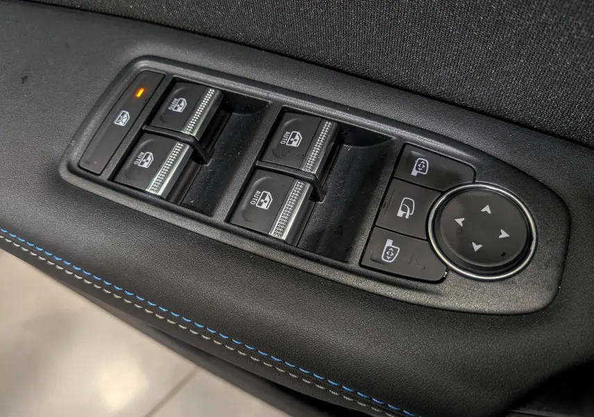 Gros plan sur les commandes de lève-vitres et rétroviseurs du côté gauche d'une Renault Symbioz gris Cassiopé avec surpiqûres bleues.