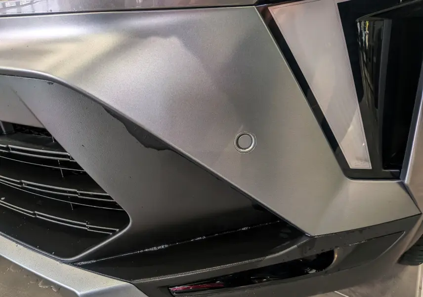 Gros plan sur le pare-chocs avant gris Cassiopé du Renault SYMBIOZ E-Tech, avec capteur de stationnement circulaire visible.