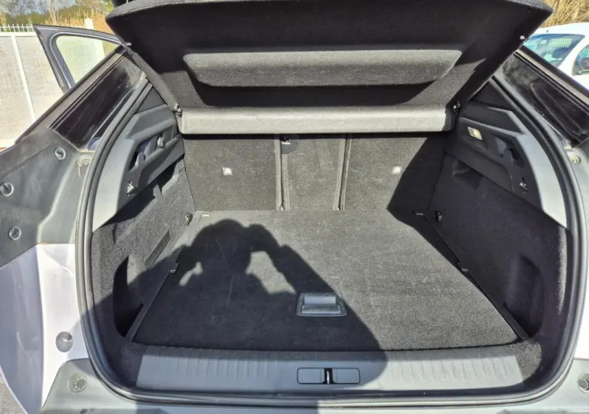 Coffre ouvert vu de l'arrière d'un Peugeot 3008 Hybrid gris clair, montrant un espace de chargement propre et spacieux.