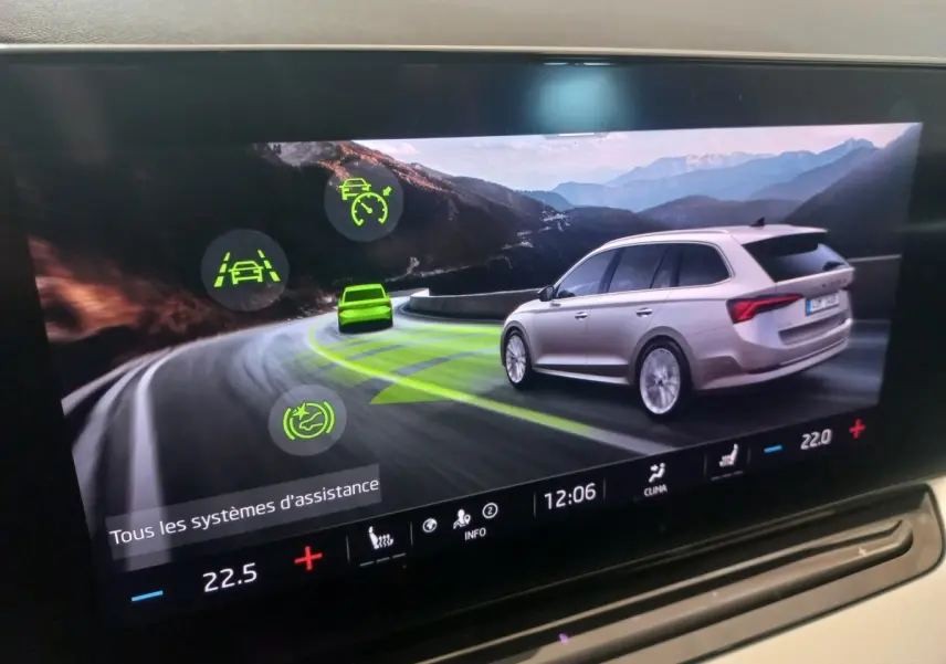 Affichage tactile montrant une Skoda Octavia beige vue de trois quarts arrière sur route de montagne sinueuse.