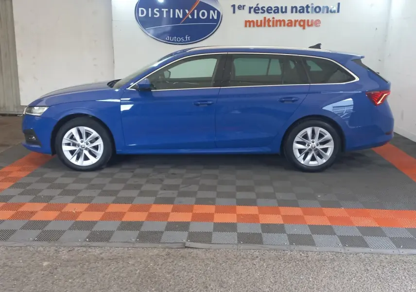 Vue de profil droit d'une Skoda Octavia break bleu 2022 stationnée en intérieur avec jantes argentées et vitres teintées.