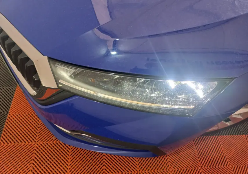 Gros plan sur le phare avant droit et la calandre d'une Skoda Octavia bleu électrique, vue en légère plongée.