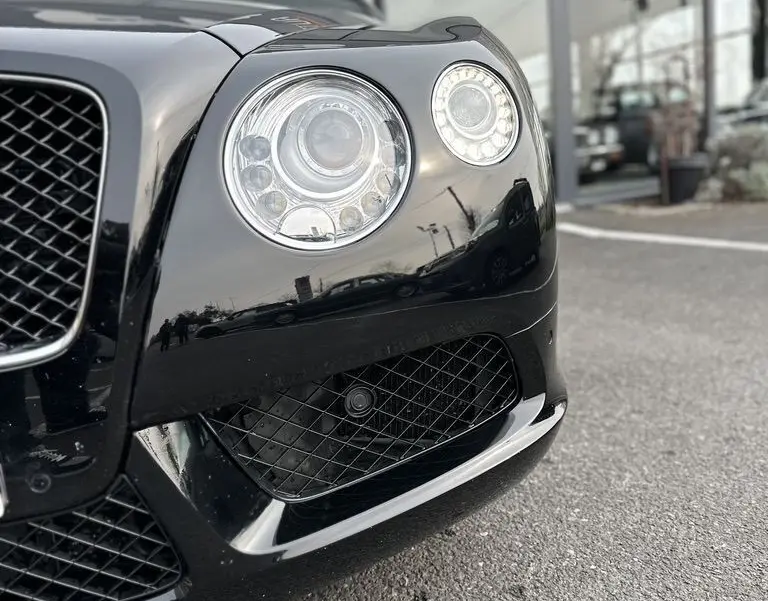 Gros plan sur le phare avant droit noir brillant d'une Bentley Continental GT 4.0 V8 Mulliner 2013, avec calandre en nid d'abeille.