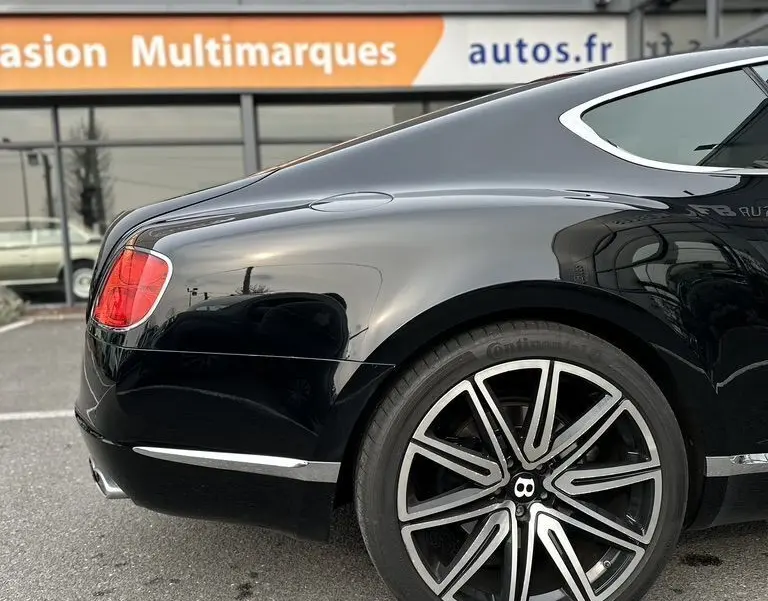 Vue arrière côté gauche d'une Bentley Continental GT Mulliner noire, mettant en valeur la jante distinctive et la ligne fluide du coffre.