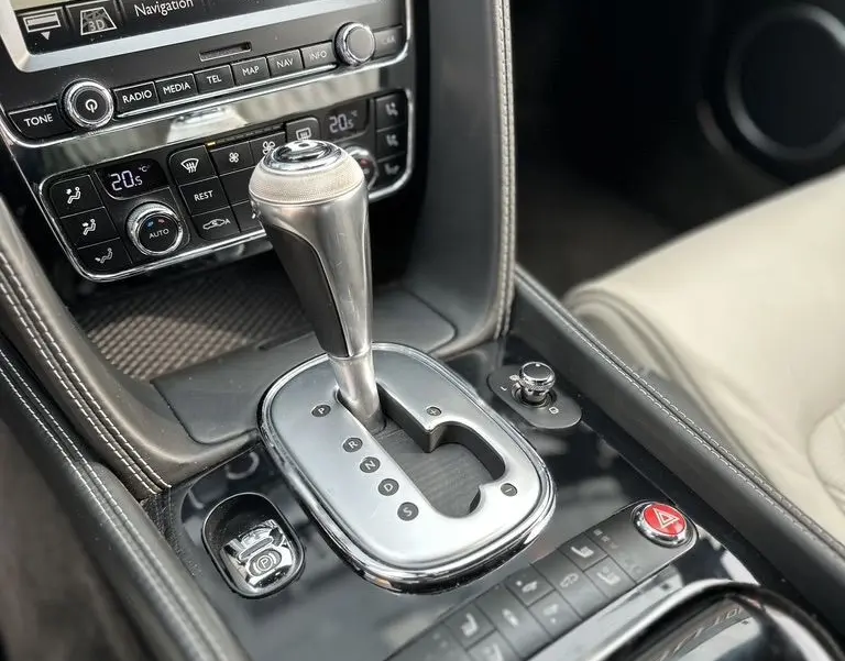 Gros plan sur la console centrale noire de la Bentley Continental GT 4.0 V8 Mulliner 2013 avec levier de boîte auto et écran navigation.