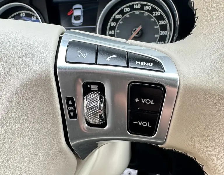 Gros plan sur le volant beige de la Bentley Continental GT Mulliner 2013, avec commandes audio et tableau de bord visible.